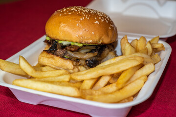  A delicious looking beef burger with french fries still in its takeout box. Although this fast food tastes good, it isn't healthy and is known to increase cholesterol among other negative effects