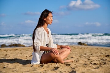 Fototapeta na wymiar Young beautiful woman in lotus position meditating on the beach