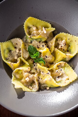 Italian ravioli dumpling on grey plate with herbs and cheese on the table