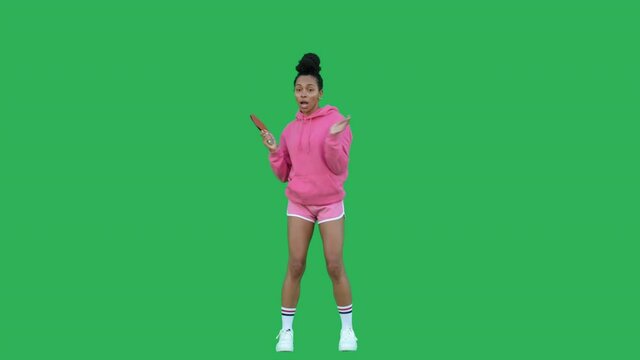 Young woman table tennis player over green background. Pretty girl wearing pink hoodie and shorts dancing and having fun with racket. Chroma key. Copy space. 4k raw video footage