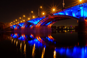 Fototapeta premium Blue and golden lights of illuminated Communal bridge over the Yenisei River in Krasnoyarsk, Russia. Reflection of a bridge and illuminations in the water. Night urban landscape. City Light