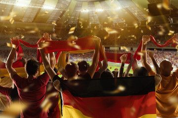 Back view of football, soccer fans from Germany cheering their team with black red yellow flags and scarfs at stadium.
