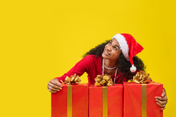 mujer afroamericana abrasando regalos de navidad en fondo amarillo 