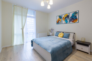 Interior of a small bedroom in a modern minimalist style, in light colors, a large bed with a blue blanket