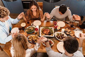 Multiracial friends holding hands and praying during thanksgiving dinner