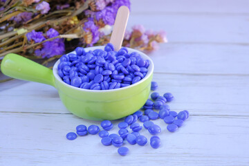 violet depilatory wax granules are scattered on a Wooden background and in the green bowl with a...