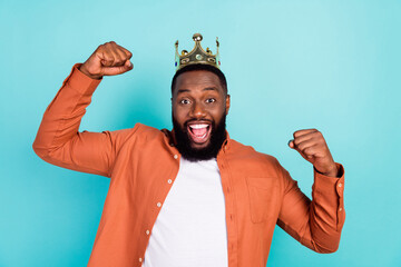 Photo of young afro man happy positive smile rejoice victory success wear crown isolated over teal...