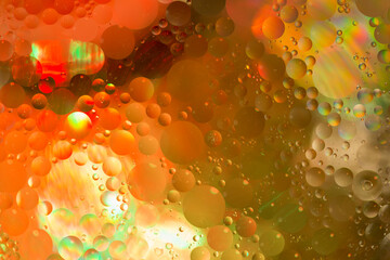 Abstract background of bright coloured bubbles of oil on water. Hues of orange, yellow, green,...
