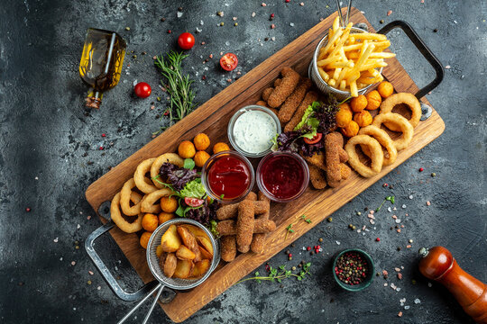 fast food meals mozzarella sticks, onion rings, french fries, chicken nuggets and sauce. pub appetizers on a wooden board. banner, menu, recipe place for text, top view