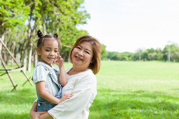 Happy little cute girl on a piggyback ride with her grandmother playing together in the summer park...