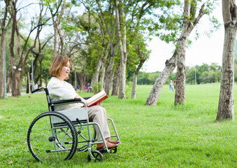 Asian elderly patient woman injured arm wrapped in cast sitting on wheelchair and reading a book in...