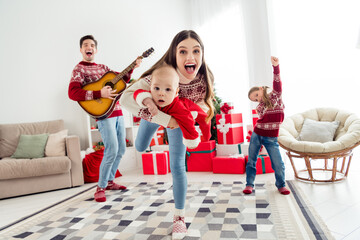 Photo of positive ecxited couple two kids dressed new year pullovers smiling playing guitar dancing indoors house home room