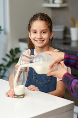 Obraz na płótnie Canvas Closeup portrait of a mom pours her cute smiling daughter milk for breakfast