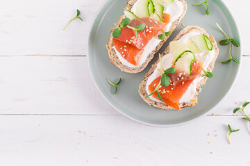 Toasts or open sandwiches with salted salmon, ricotta cream cheese, cucumber, sprouts and whole grain bread on white table. Healthy food, diet. Breakfast. Top view.