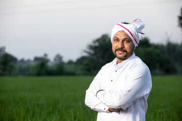 Happy rural Indian mustache man farmer giving side pose standing in field with hands crossed...