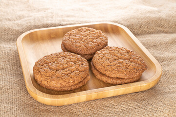 Several sweet oatmeal cookies on a bamboo tray, close-up, on sacking.