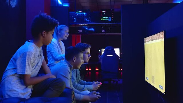 Group young multiethnic diverse teen sit in cybercafe use pc play on-line sport videogame in dark room, feel happy celebrate victory winning competition. E-sport activity, gen z tech addiction concept