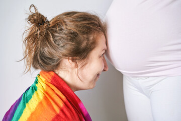Young woman hearing pregnant belly. Second mother with unborned child. LGBT girls concept. Happy...