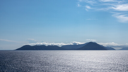 Blue Ionian sea landscape view on Lefkada Greece island. Bright day with low clouds over distant islands and contrast sunbeam on water