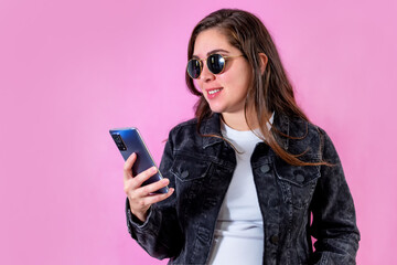 Naklejka premium Young woman over isolated pink background sending a message with the mobile