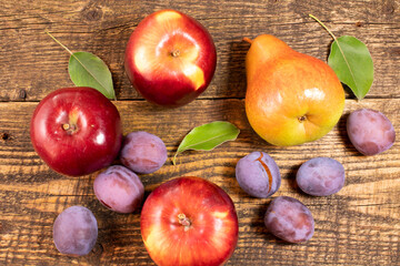 Fresh fruit lying on a wooden table.Apples, pears, fresh leaves and plums on a wooden background.