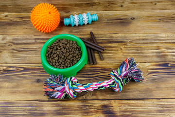 Dog toys and feed for dogs in green plastic bowl on wooden background. Dog care concept