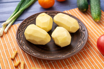 Raw peeled potato tubers on a plate on the kitchen table with vegetables. Preparation for cooking.