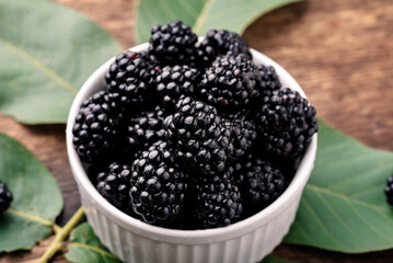 Fresh berries of blackberries in a white bowl on a wooden background close-up.