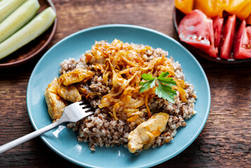 Buckwheat porridge with meat, onions and carrots on a wooden background. With fresh vegetables, cucumbers and tomatoes.