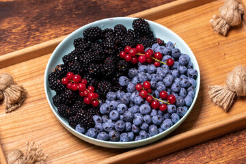 mix of fresh berries - blueberries, blackberries and red currants in a plate on a wooden tray. Fruit, berry background.