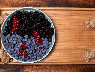 mix of fresh berries - blueberries, blackberries and red currants in a plate on a wooden tray. Fruit, berry background.