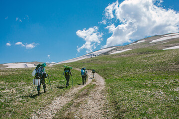 a group of people goes hiking with backpacks in mountains Caucasus, bright blue sky, valley with snow