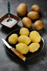 peeled potatoes on black plate - gray background - closeup