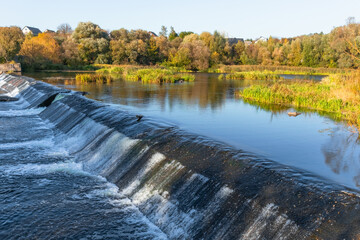 View of a small dam on the river on a sunny autumn day.