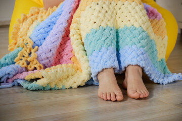 A young woman knits a warm bright plaid from multi-colored terry looped yarn with her hands. A cozy pastime for a hobby