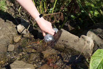 Woman taking water from forest spring on hiking trip. Hiker pours water. Volunteer pulls a bottle out of the water, during the event to clean the river. Earth day and environmental improvement concept