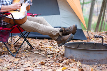 Man in hiking boots playing guitar at a campsite