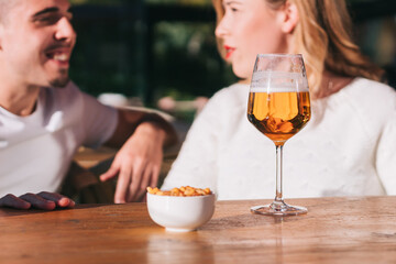 Close-up of a glass of beer on the table of a bar, restaurant or cafeteria. with a group of friends talking happily and smiling.