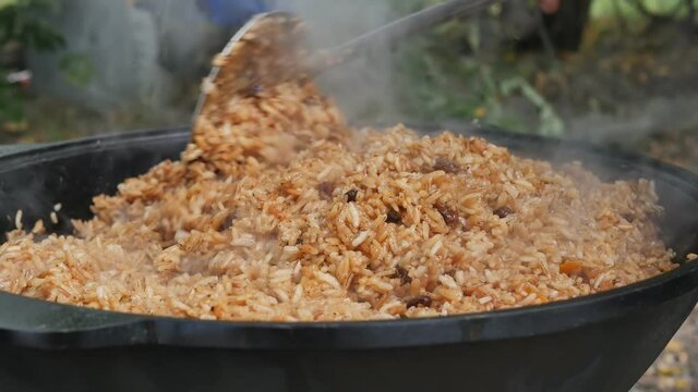 the cook evens and mixes rice pilaf in a large cast-iron pot with a metal slotted spoon. The final stage of the readiness of the Uzbek pilaf. Slow motion