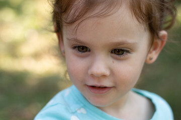 Portrait of a beautiful young girl in a blue t-shirt on a blurred green natural background. Outdoor photo
