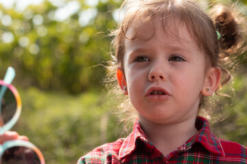 Beautiful blonde curly little girl in a red plaid shirt on a blurred natural background