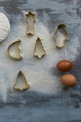 Christmas baking dishes for Santa Claus figurines, Christmas tree, moon, stars, bells on snow scattered flour, eggs and flour are prepared for baking festive New Year's cookies.