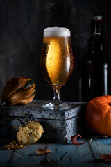 Glass of beer with moisture drops on the glass and pumpkin on a wooden table