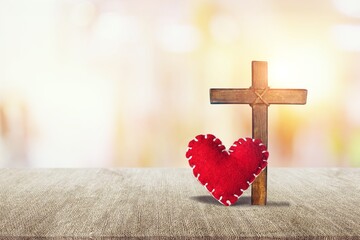 Red heart with a wooden Christian cross on floor in the morning light,