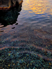 Coastal sea stones and crystal clear water evening. Sea surface illuminated by clear water. Rock bottom seen below clear water in mountain lake. Splash and reflections Sunset on ocean surface