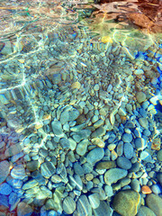 Coastal sea stones and crystal clear water at sunny day. Sea surface illuminated by clear water. Rock bottom seen below clear water in mountain lake. Splash and reflections on ocean surface
