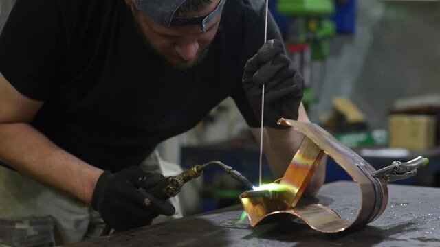 Metalwork craftsman working with metal using burner tool. Worker man in protective gloves working in the workshop. Do it yourself. Small local business.