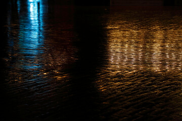 Modern luxury texture. Multi-colored dark background from reflection on wet stone. Blue and yellow on a dark base. Underlay for text. A versatile dark beautiful cobblestone pavement. Wet road 