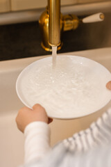 A little girl helps with household chores in the kitchen. Washes and puts clean dishes.