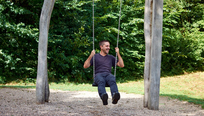 A young Hispanic man sitting on a swing in a park